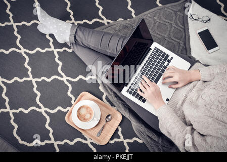 Young creative woman sitting in the floor and working with laptop, cup of coffee and mobile phone, top view Stock Photo