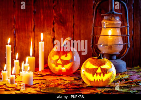 Halloween pumpkin with glowing face on a wooden background with many flaming candles, an antique lantern and autumn leaves. Idea for flyers, poster, p Stock Photo