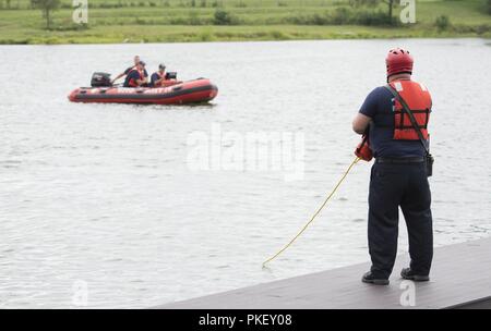 A firefighter holds a rope tied to divers from the 788th Civil Engineer Fire Department, as they search for a reported drowning subject as part of a base exercise at Wright-Patterson Air Force Base, Ohio, July 31, 2018. Exercises are routinely held to streamline unit cohesion when responding to emergencies and test the base’s readiness to rapidly deploy. Stock Photo