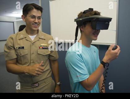 NEWPORT, R.I. (July 31, 2018) Lt. John Tanalega of Las Vegas, Nevada, an instructor assigned to Surface Warfare Officers School (SWOS), explains the Conning Officer Virtual Environment (COVE), a state-of-the-art navigation and shiphandling trainer to Parker Johnson, of Utah, a Gold Star teen during a tour at SWOS. Gold Star teens, ages 15-18, are surviving children of military personnel who lost their lives in the line of duty while serving in Army, Navy, Air Force and Marine Corps special operations units. Twenty-one teens attended a weeklong Gold Star Teen Sailing Adventure Camp at Naval Sta Stock Photo
