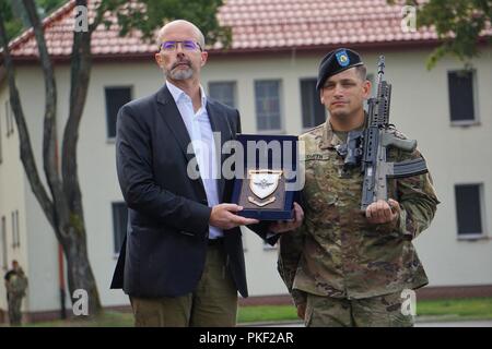 Jonathon Knot, U.K. Ambassador to Poland, presents Spc. Timothy Smith, Cavalry Scout, Quickstrike Platoon, 4th Squadron, 2d Cavalry Regiment, with an award at the Bemowo Piskie Training Area, Poland, August 3, 2018. Smith was the highest ranking member of his class in a two week British run Potential Non-Commissioned (PNCO) Candidate's Course. Stock Photo