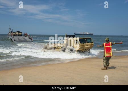 VIRGINIA BEACH, Va. (July 26, 2018) A Sailor assigned to Beachmaster Unit (BMU) 2 ground guides an U.S. Army Heavy Expanded Mobility Tactical Truck from an Improved Navy Lighterage System (INLS) Causeway Ferry operated by Amphibious Construction Battalion (ACB) 2 to the Utah Beach marshalling area during the Trident Sun 18 exercise onboard Joint Expeditionary Base Little Creek – Fort Story. Trident Sun 18 is a maritime prepositioning force (MPF) operation intended to provide training to reserve component personnel with regards to the in stream offload of military vehicles and equipment. Stock Photo