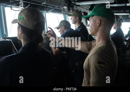 STRAIT OF HORMUZ (August 8, 2018) Lt. j.g. Simonas Vollmer, of the German navy, stands officer of the deck watch as  the guided-missile destroyer USS The Sullivans (DDG 68) conducts a routine transit through the Strait of Hormuz. The Sullivans is deployed to the U.S. 5th Fleet area of operations in support of naval operations to ensure maritime stability and security in the Central region, connecting the Mediterranean and the Pacific through the western Indian Ocean and three strategic choke points. Stock Photo