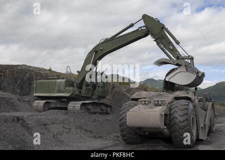 Sgt. Eric Jerabek, a heavy equipment operator with Headquarters Battery, 14th Marine Regiment, 4th Marine Division unloads gravel from an excavator into a wheel tractor-scraper to be laid onto the runway during Innovative Readiness Training, Old Harbor, Alaska, Aug. 5, 2018. This year marks the completion of the 2,000-foot extension of Old Harbor’s runway. Stock Photo