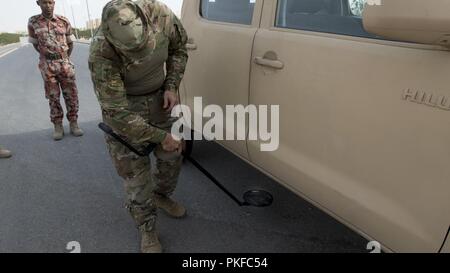 U.S. Army Staff Sgt. Christopher Reitz, a team lead assigned to the 157th Military Engagement Team, Wisconsin Army National Guard, attached to U.S. Army Central, utilizes a mirror to search underneath a suspect vehicle at a vehicle control point practical exercise held in Haima, Oman, Aug. 8, 2018. During the practical exercise Soldiers from 157th MET and the Royal Army of Oman's Border Guard Brigade shared their preferred techniques and methods to conduct border security to strengthen both country's defensive capabilities. Stock Photo