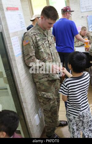 DONGDUCHEON, Republic of Korea –Cadet Michael Bertlesman, a rising senior political science major at the Rochester Institute of Technology from Plainview, New York, and Cadet Troop Leadership Training program participant assigned to the 6th Battalion, 37th Field Artillery Regiment, accepts a candy offering from a student at an orphanage July 31st. Bertlesman accompanied his sponsor 2nd Lt. Seth Maddy, a fires platoon leader with 6-37th FAR. Soldiers attending the orphanage removed their shoes and wore sandals as is customary in the Republic of Korea. Stock Photo