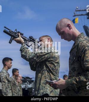 PACIFIC OCEAN - U.S. Marine Lt. Col. Matthew Danner, commanding officer, Battalion Landing Team 3/1, 13th Marine Expeditionary Unit (MEU), inspects his Marine's M4 carbine aboard the Wasp-class amphibious assault ship USS Essex (LHD 2) during a regularly scheduled deployment of the Essex Amphibious Ready Group (ARG) and the 13th MEU, July 31, 2018. The Essex ARG/13th MEU team is a capable and lethal Navy-Marine Corps team deployed to the 7th fleet area of operations to support regional stability, reassure partners and allies and maintain a presence postured to respond to any crisis ranging fro Stock Photo