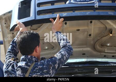 An Iraqi Federal Police member inspects under the vehicle’s hood during vehicle search class at Camp Dublin, Iraq, Aug. 06, 2018. The curriculum at enhanced partner capacity sites includes: leadership, ethics and law of war training and instruction. Additionally, the recruits are taught land navigation, basic medical training, infantry skills and small unit tactics. Stock Photo