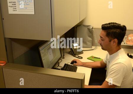 SANTA RITA, Guam (Aug. 10, 2018) - Tadd Oshiro, a mechanical engineer from the engineering and planning department at Pearl Harbor Naval Shipyard, works at the Ship Support Office onboard Polaris Point, Aug. 10. Oshiro, part of a team of Pearl Harbor Naval Shipyard engineers temporarily assigned to the Guam Maintenance Team, troubleshoots jobs for the machinery repairmen in the repair department aboard the submarine tender Frank Cable (AS 40). Prior to the Pearl Harbor Naval Shipyard team's arrival Frank Cable's repair department did not have access to this level of troubleshooting expertise.  Stock Photo