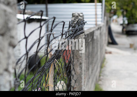 Broken wire fence with blurred concrete fence and street in the background Stock Photo