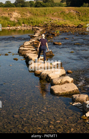 UK, Yorkshire, Wharfedale, Grassington, woman using stepping stones across River Wharfe during dry summer weather Stock Photo