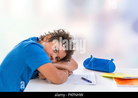 Overwhelmed schoolboy. Bored and tired teenage boy doing homework on desk in his room,seems sleepinp Stock Photo