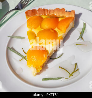 Slice of a French Baked Custard Tart with apricots and rosemary on a white plate - Flan parisien Stock Photo