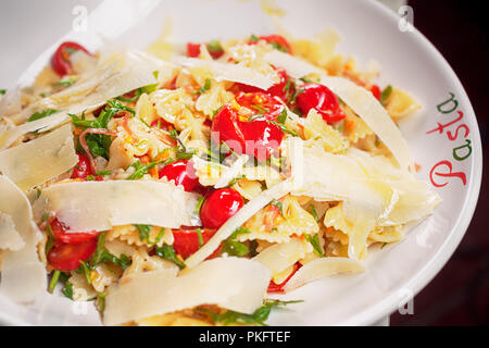 Pasta with Prosciutto, tomato, rocket and Parmesan Cheese, horizontal, wine glass in background Stock Photo