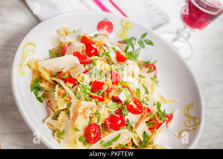 Pasta with Prosciutto, tomato, rocket and Parmesan Cheese, horizontal, wine glass in background Stock Photo