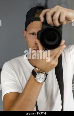 handsome man with freckles holds a digital camera and takes pictures. The concept of a young successful photographer Stock Photo