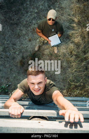 overhead view of african american tactical instructor with notepad examining young soldier during obstacle run Stock Photo