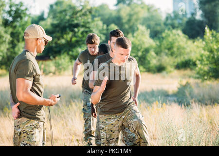 tactical instructor with stop watch examining multiracial soldiers during obstacle run on range Stock Photo