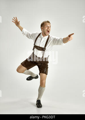 Portrait of Oktoberfest young man in hat, wearing a traditional Bavarian clothes standing at full-length at studio. The celebration, oktoberfest, festival concept Stock Photo