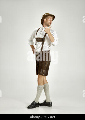 Portrait of Oktoberfest young man in hat, wearing a traditional Bavarian clothes standing at full-length at studio. The celebration, oktoberfest, festival concept Stock Photo