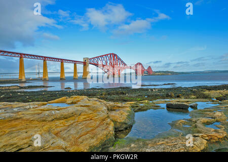 FORTH RAILWAY BRIDGE SCOTLAND OVER THE FIRTH AT LOW TIDE WITH LARGE WEATHERED ROCKS ON THE BEACH Stock Photo