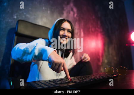Woman in the hood sitting and working at laptop as hacker. Running malware program on computer in the internet with malevolent smile on her face. Stock Photo