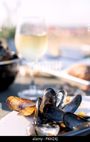 Mussels in a saucepan and a glass of cold white wine. Delicious seafood dinner in a restaurant on the beach. Copy space. Stock Photo