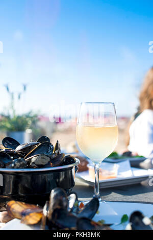 Mussels in a saucepan and a glass of cold white wine. Delicious seafood dinner in a restaurant on the beach. Copy space