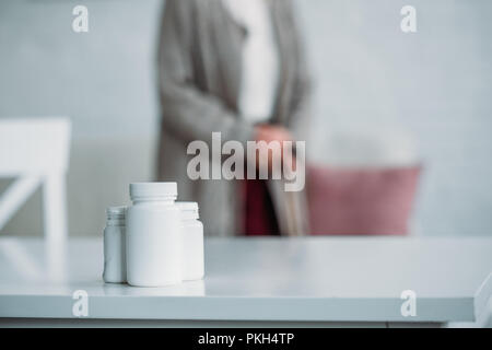 selective focus of senior woman with walking stick standing in room with medicines on tabletop at home Stock Photo