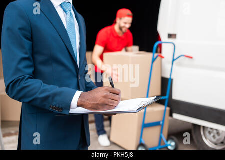 partial view of african american businessman making notes with caucasian delivery man working behind Stock Photo