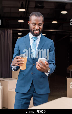 portrait of smiling african american businessman with coffee to go and smartphone