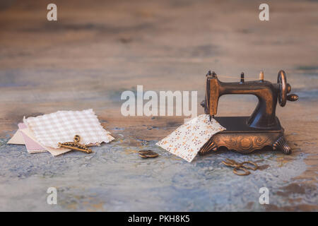 Vintage mini sewing machine with scissors, buttons and fabric on rustic background, toned Stock Photo