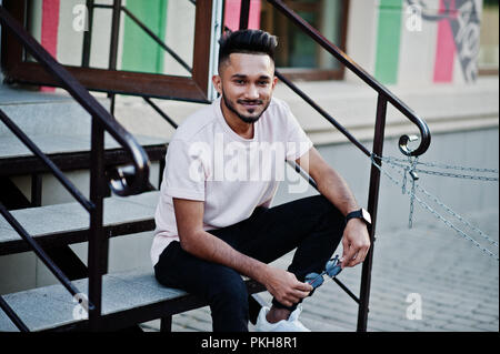 Stylish indian beard man at pink t-shirt. India model sitting on stairs outdoor at streets of city. Stock Photo