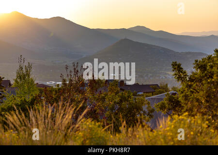 Sunset on mountains behind homes and trees Stock Photo
