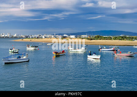 Fishing boats anchoring in river estuary with sandbank, green hill and city in the background Stock Photo