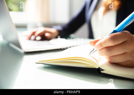 Close-up Of A Businesswoman's Hand Writing Note With Pen In Diary Over Desk Stock Photo