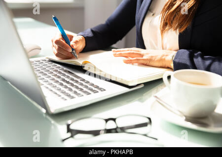 Close-up Of A Businesswoman's Hand Writing Note With Pen In Diary Over Desk Stock Photo