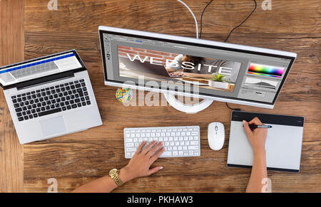 Female Designer's Hand Using Graphic Tablet While Creating Website On Computer Stock Photo