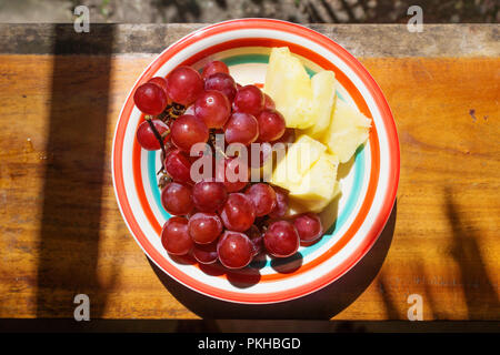 Fresh red grapes and pineapple slices on colored plate, Guatemala Stock Photo