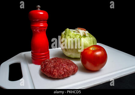 Raw hamburger, tomato, lettuce and salt over a white tablet - isolated on black background Stock Photo