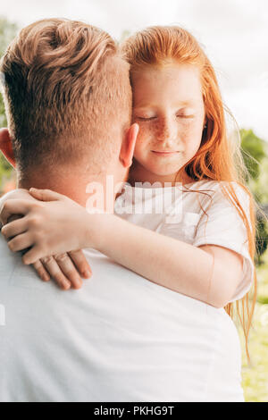 adorable redhead child with closed eyes hugging father at park Stock Photo