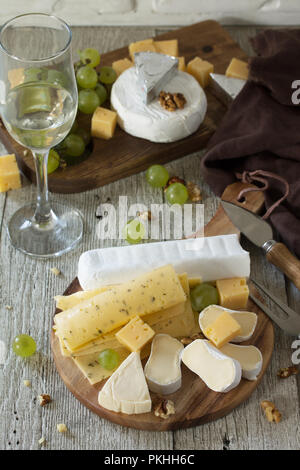 Assortment of cheeses, wine glass and nuts on a wooden table. Stock Photo