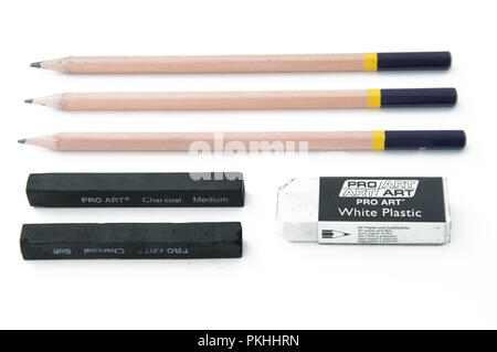 Three drawing pencils beside an rubber eraser and charcoal sticks on a white background. Stock Photo