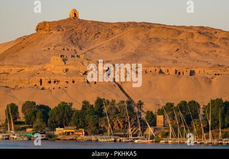 Hilltop Muslim prophet tomb Qubbet el-Hawa in early morning above ancient rock cut tombs with felucca sailing boats, Nile River, Aswan, Egypt, Africa Stock Photo