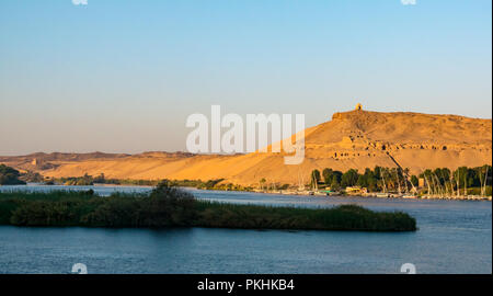 Aga Khan mausoleum and hilltop Qubbet el-Hawa tomb in early morning light with traditional felucca sailing boats, Nile River, Aswan, Egypt, Africa Stock Photo