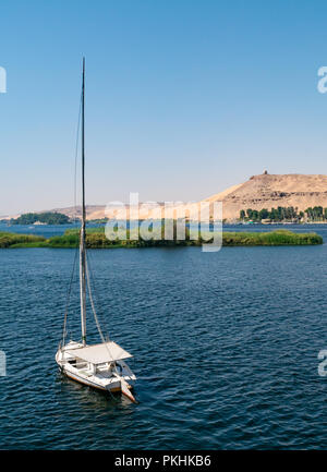 Traditional felucca sailing boat and view of hilltop tomb of Muslim prophet, Qubbet el-Hawa on sand cliff, Nile River, Aswan, Egypt, Africa Stock Photo