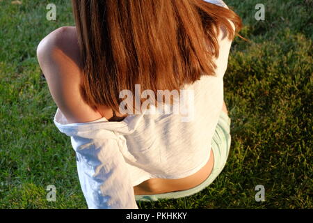 Rear view of redhair teen girl sitting on grass Stock Photo