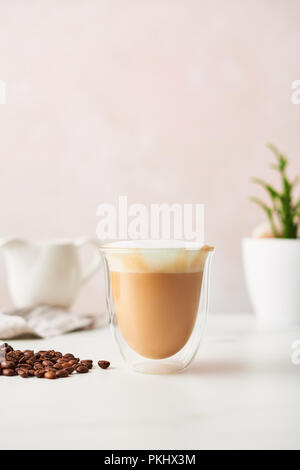Cappuccino in a double walled glass with roasted coffee beans. Feminine rose background with copy space. High resolution image. Stock Photo