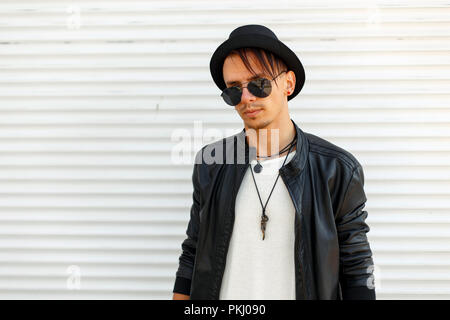 Handsome young man in stylish clothes with sunglasses posing near white metal wall Stock Photo