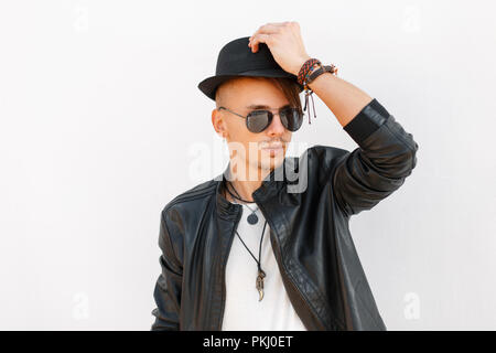Trendy handsome young man with hat and sunglasses in a black stylish jacket on a white background Stock Photo
